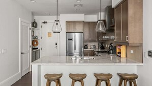 Eine moderne Küche mit Kochinsel, Edelstahlgeräten, Pendelleuchten und Holzbarhocker.
