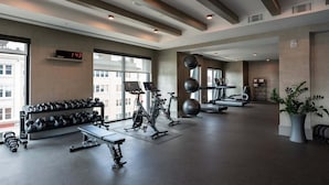 Ein modernes Fitnessstudio mit Trainingsgeräten, großen Fenstern und einer digitalen Uhr.