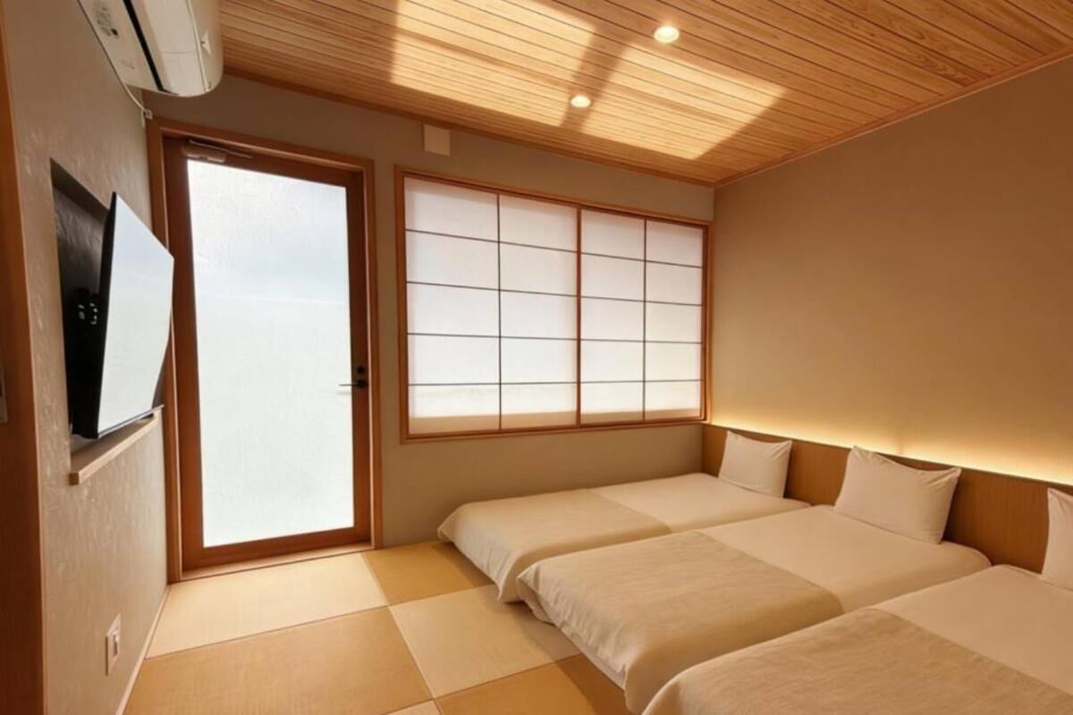 Une chambre d’hôtel avec un sol recouvert de tatamis, une porte coulissante, une grande fenêtre avec des panneaux de shoji et un téléviseur à écran plat.