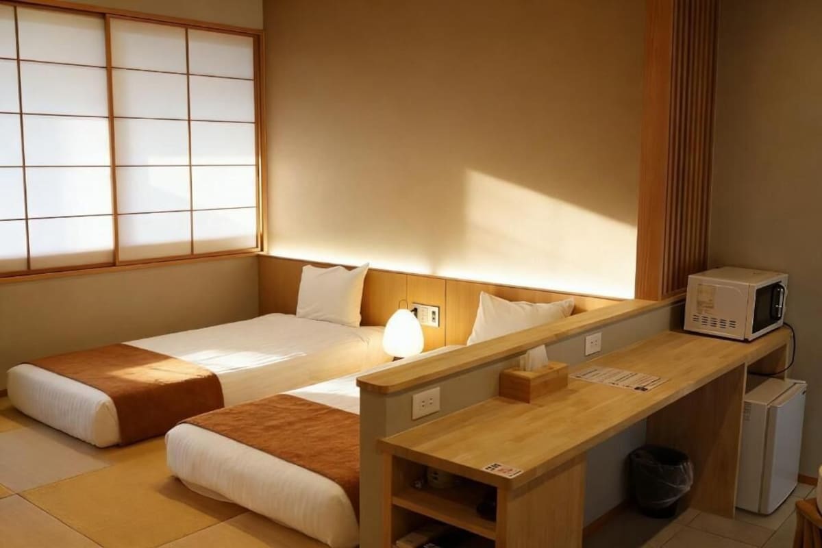 A hotel room with two beds, a wooden desk, a microwave, and a small refrigerator.
