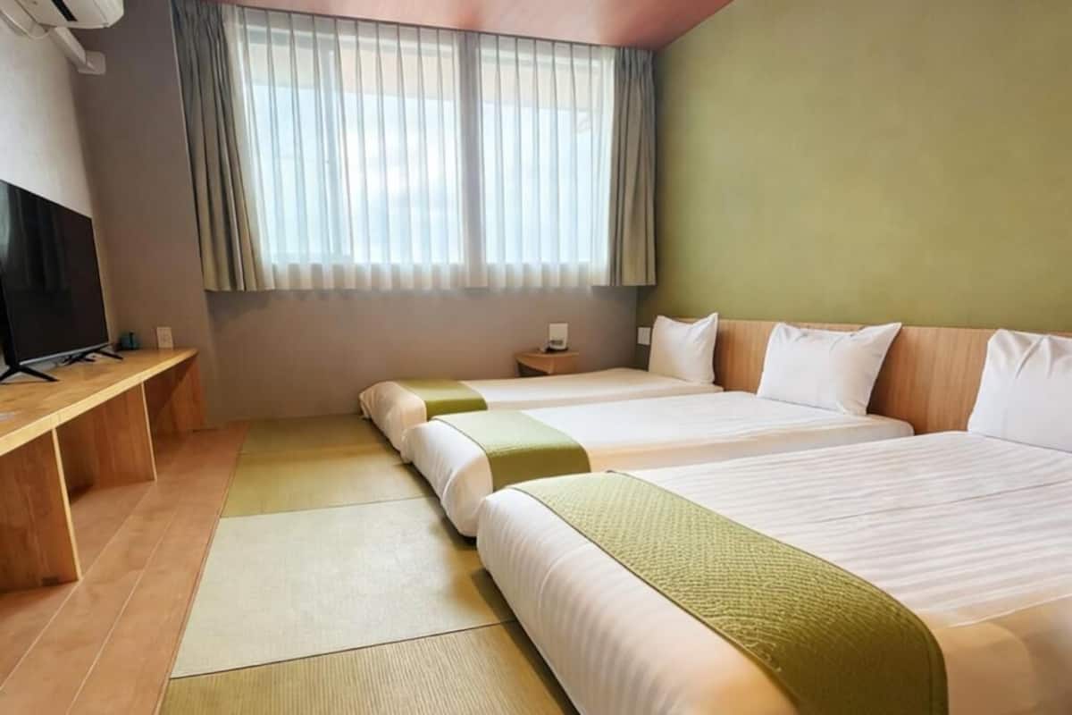 Une chambre d’hôtel avec deux lits, une télévision, un bureau et une fenêtre avec des rideaux.