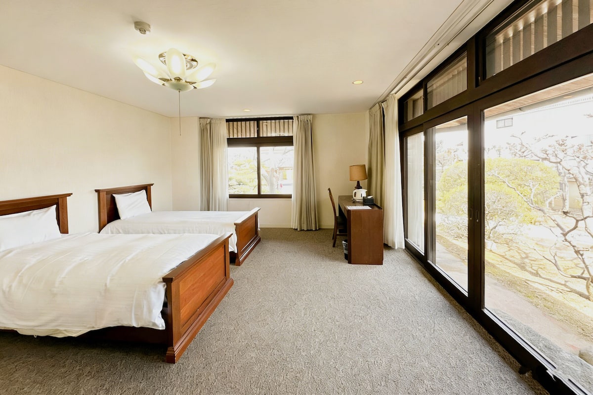 Une chambre d’hôtel avec deux lits, un bureau, une lampe et une grande fenêtre donnant sur un beau paysage.
