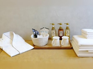 A neatly arranged bathroom with toiletries, towels, and a folded robe. - Kansai Airport Hotel Pine Villa  (Izumisano)