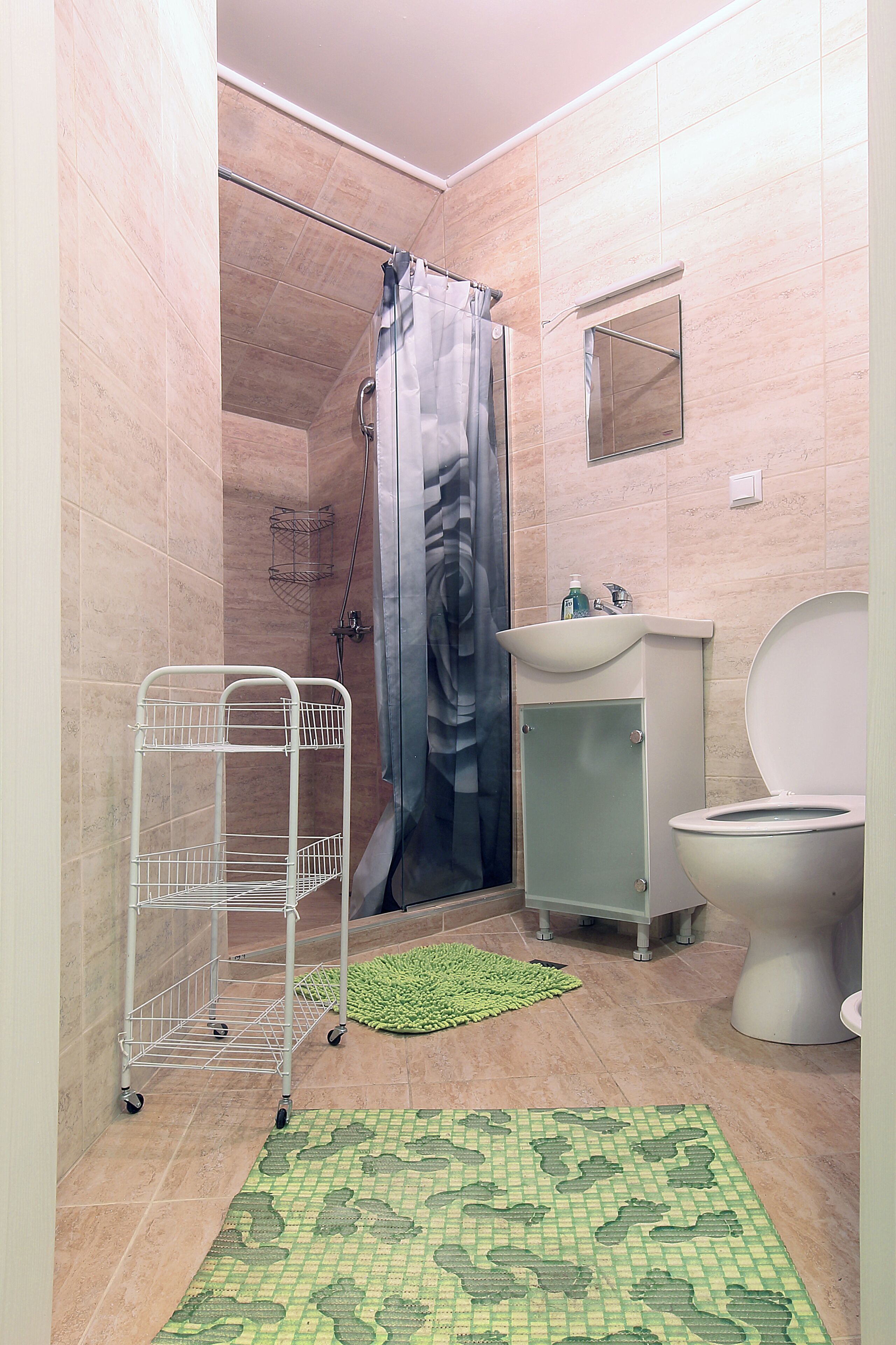 A bathroom with a shower, toilet, sink, and a metal rack.