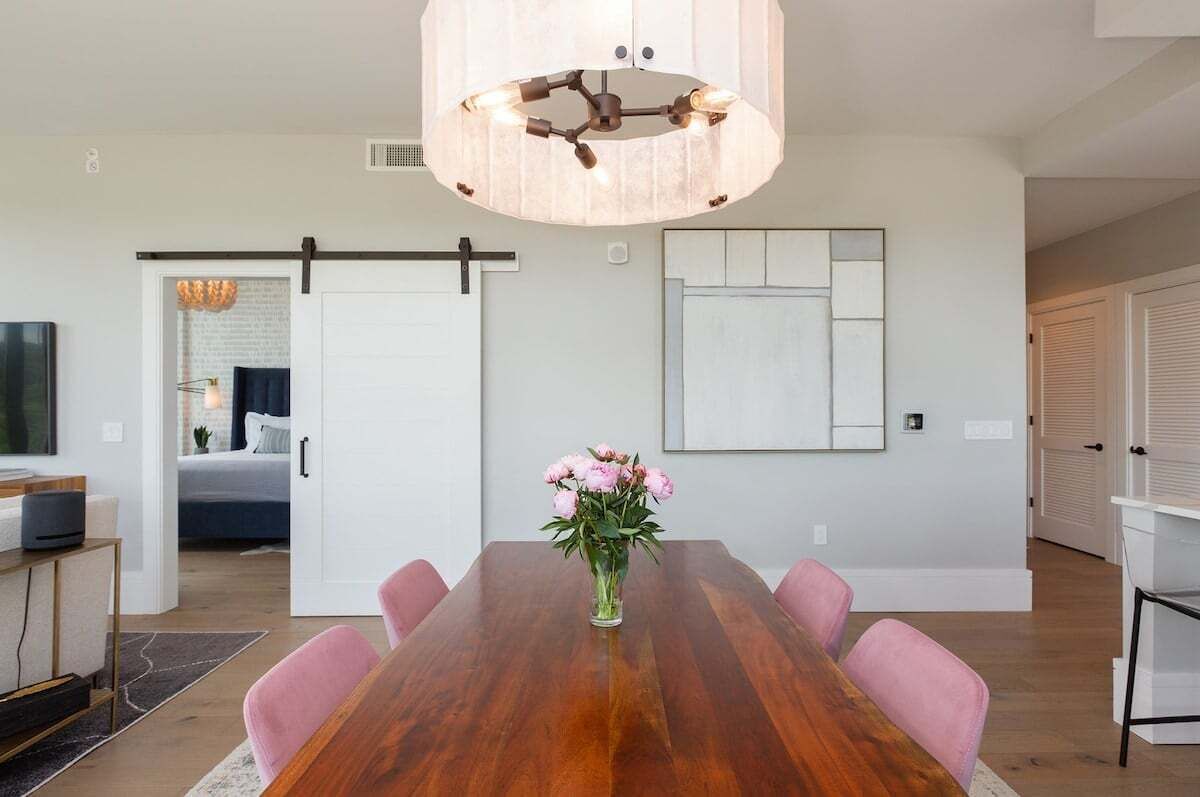 A dining area with a wooden table, pink chairs, a vase of flowers, and a modern pendant light.