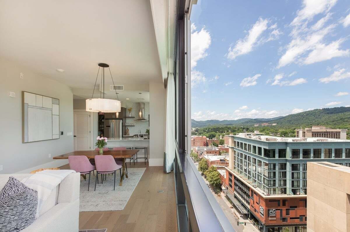 A modern apartment with a dining area, kitchen, and large windows overlooking a cityscape and hills.