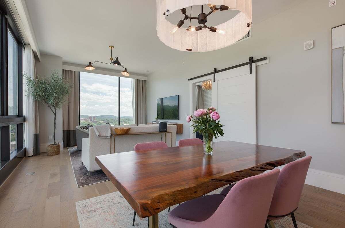 Ein zeitgemäßer Essbereich mit einem Holztisch, rosa Stühlen und einer Kronleuchter.
