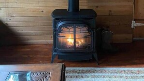 A wood-burning stove with a chimney, a power outlet, and a window with a view of trees. - Two Houses, Twice the Fun (Glacier County)