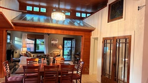 A dining area with a table, chairs, a chandelier, and a view of the outdoors through windows. - The Bell Moon Cottage | Half a Block from Downtown (Black Mountain)