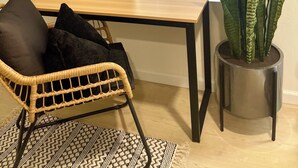 Ett rum med ett träbord, en flätad stol, en krukväxt och ett fönster med persienner.