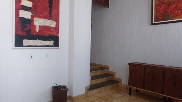 A staircase leading to a landing with a red abstract painting above it, a potted plant on the landing, and a wooden cabinet on the right.
