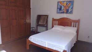A bedroom with a wooden bed, a wardrobe, a painting on the wall, and a small table with a chair.