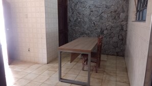 A small room with a tiled floor, a wooden table with metal legs, a stone wall, and a window with a metal bar.