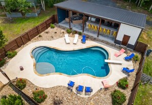 A swimming pool with lounge chairs, a covered patio, and a small building with a metal roof.