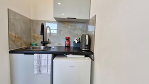 Eine kleine Küchenzeile mit Spüle, einer Kaffeemaschine, einem kleinen Kühlschrank und einem Handtuch an der Tür.