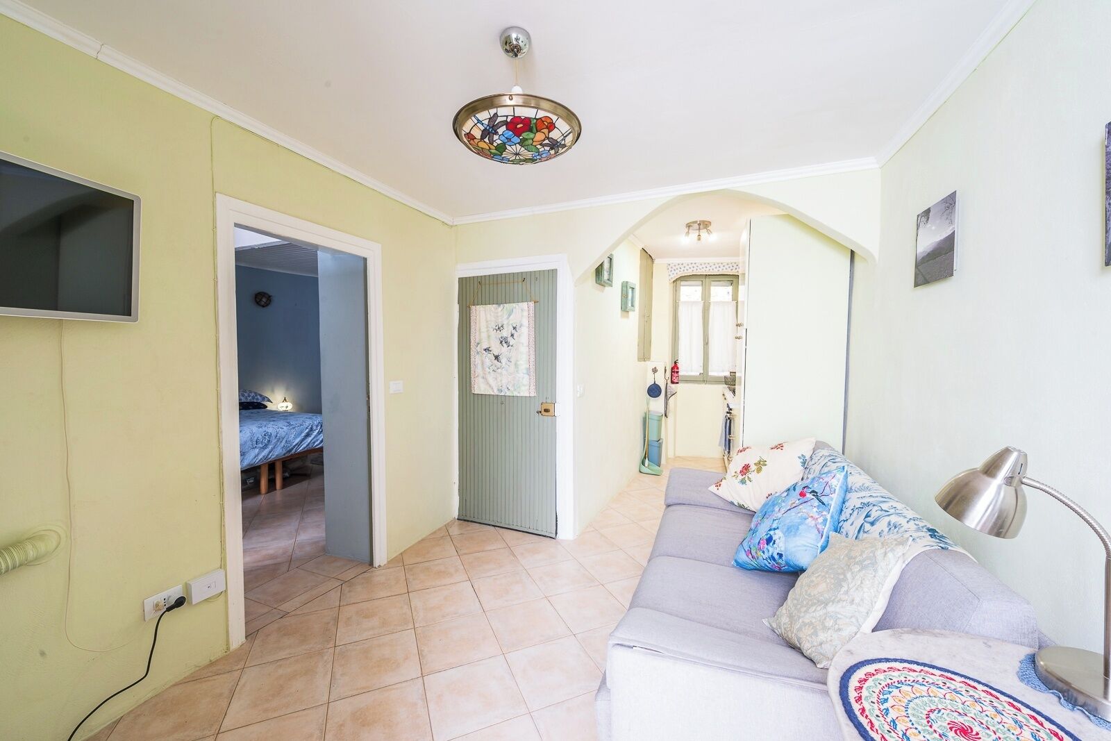 Un salon comprenant un canapé, un téléviseur fixé au mur, un ventilateur de plafond et une porte donnant sur une autre pièce.