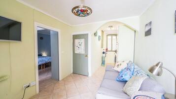 Un salon comprenant un canapé, un téléviseur fixé au mur, un ventilateur de plafond et une porte donnant sur une autre pièce.