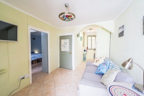 Un salon comprenant un canapé, un téléviseur fixé au mur, un ventilateur de plafond et une porte donnant sur une autre pièce.