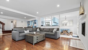 Una sala de estar amplia con un sofá seccional gris, una mesa de centro de madera y un comedor con mantel a rayas.