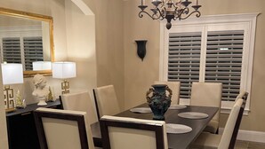 A dining room with a dark wooden table, beige chairs, a chandelier, and a vase on the table. - Home With A View, Beautiful 3 Bedroom 4 Bath, Each Bedroom with Private Bath (Redding)