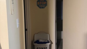 Un couloir étroit avec un panier à linge, un panneau de signalisation indiquant un arrêt et un thermostat fixé au mur.