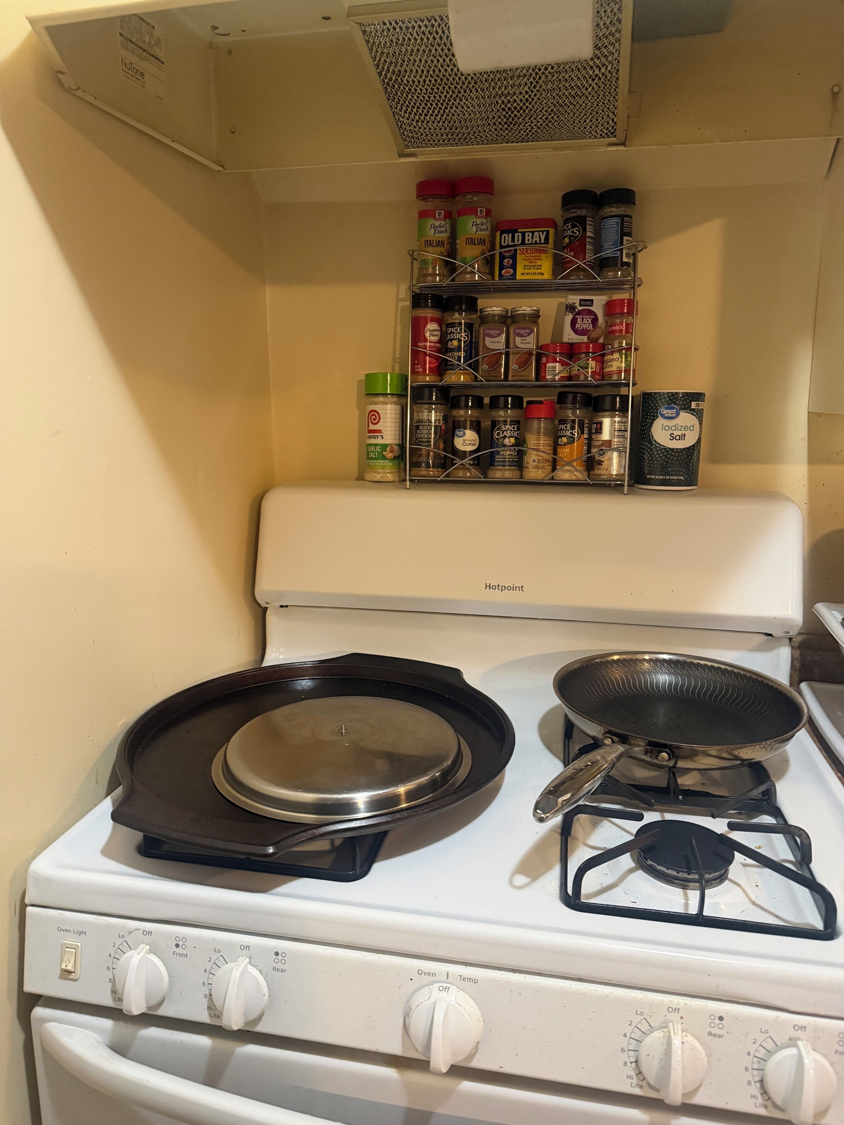 A kitchen with a stove, a frying pan, and a spice rack.