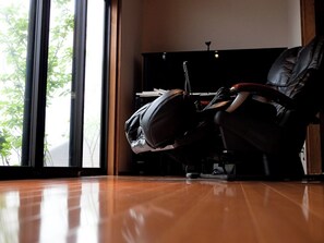 Una habitación con piso de madera, un sillón de cuero negro y una unidad de entretenimiento negra.