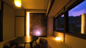 A room with tatami flooring, a low table with cushions, and a view of the outside through large windows. - Yamadaya (Beppu)
