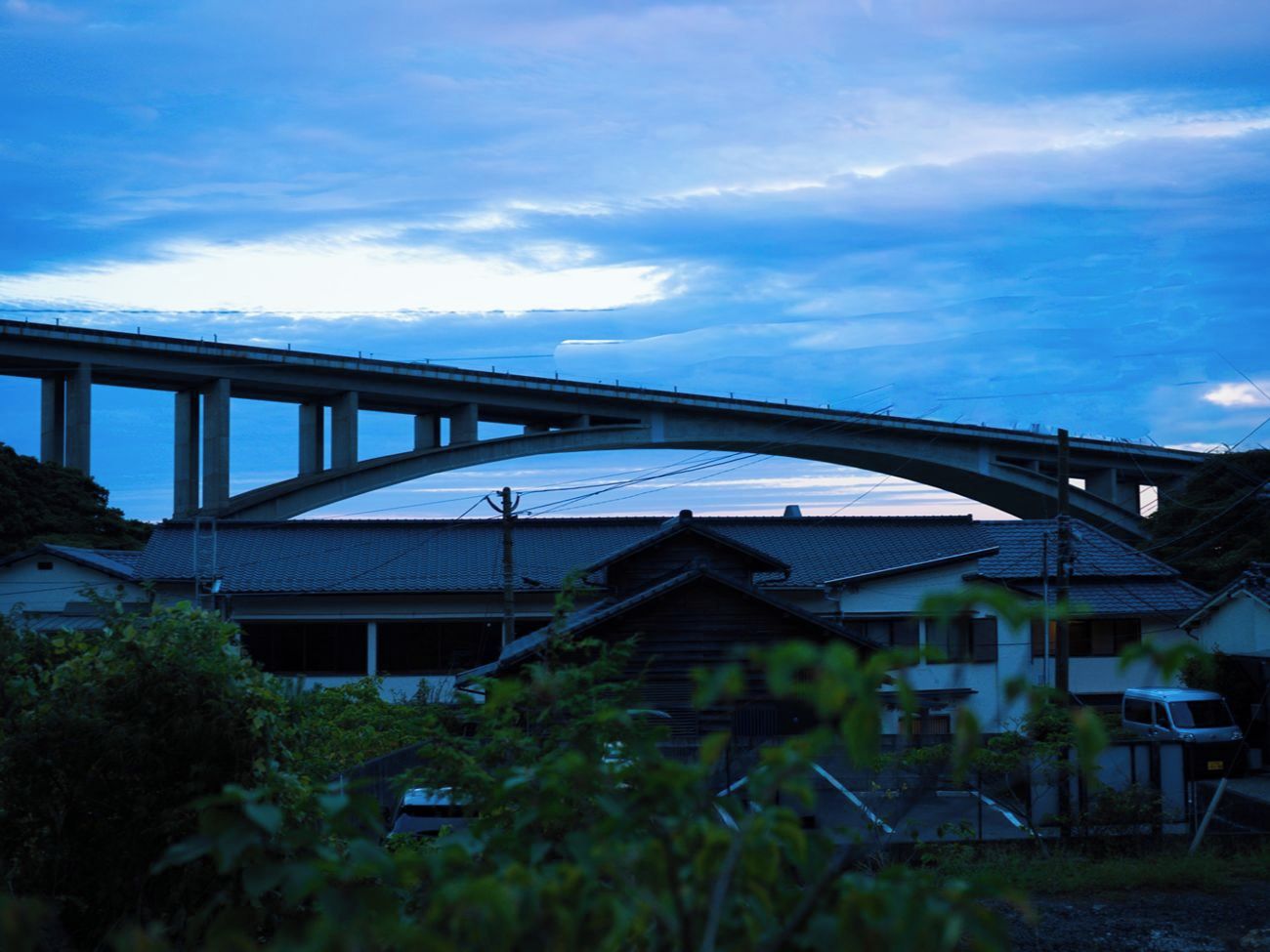 A bridge over a building with a traditional roof, surrounded by greenery.