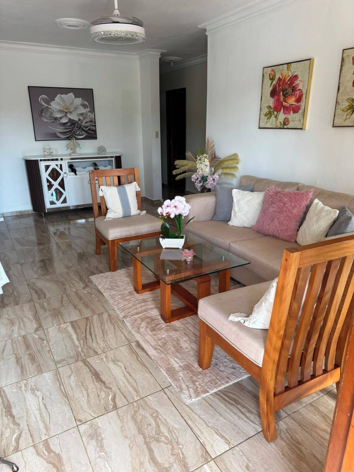 A living room with a sofa, two wooden chairs, a glass coffee table, and a decorative vase.