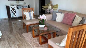 A living room with a sofa, two wooden chairs, a glass coffee table, and a decorative vase.