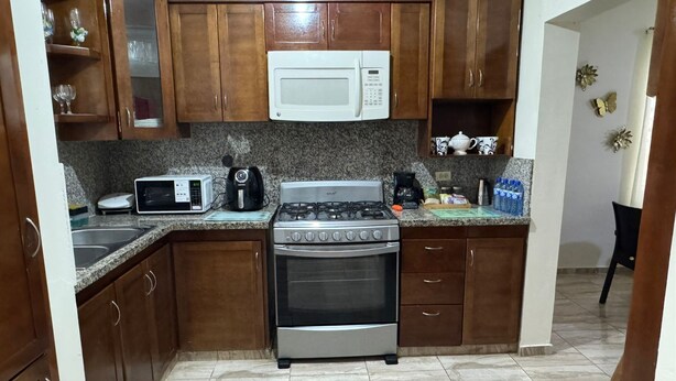Una cocina con gabinetes de madera, microondas, estufa y pileta.