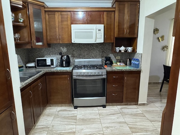A kitchen with wooden cabinets, a microwave, a stove, and a sink. - A Tropical Getaway at La Caoba (San Francisco de Macorís)