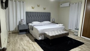 Un dormitorio con cama, mesitas de noche, alfombra negra, ventilador de techo y decoración de mariposas en la pared.