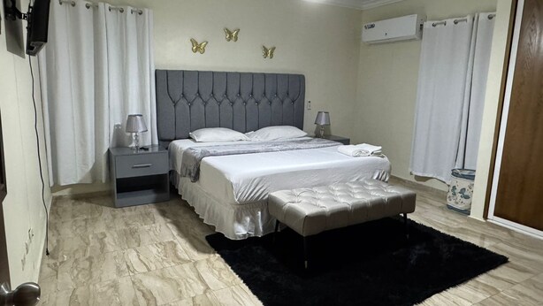 Une chambre à coucher avec un lit, des tables de chevet, un tapis noir, un ventilateur de plafond et des décorations murales représentant des papillons.