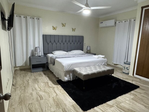 A bedroom with a bed, nightstands, a black rug, a ceiling fan, and decorative butterfly wall art. - A Tropical Getaway at La Caoba (San Francisco de Macorís)