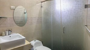 Un baño con lavamanos, inodoro, espejo y ducha con mampara de vidrio.