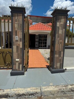 A gated entrance with a paved pathway leading to a building with a red-tiled roof.
