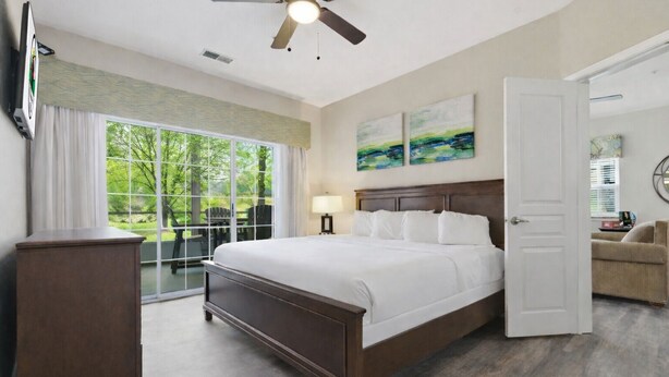 Ein Hotelzimmer mit einem großen Bett, einem Deckenventilator, Blick durch eine Glastür und Kunstwerken an der Wand.