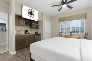 A bedroom with a bed, a ceiling fan, a window with blinds, and a kitchenette with cabinets and appliances. - 2 BR Golf Course View Condo, Outdoor Pool, Discounted Golf Rounds, Dog Friendly (Branson)