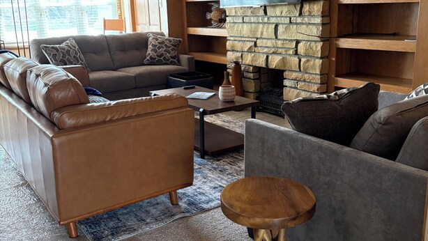 A living room with a stone fireplace, leather sofas, a coffee table, and a flat-screen TV mounted on the wall. - 2-bedroom duplex in Mt. Washington on quiet family street near Grandview Ave. (Pittsburgh)
