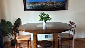 A dining area with a round wooden table, four chairs, a potted plant, and a cityscape painting on the wall. - 2-bedroom duplex in Mt. Washington on quiet family street near Grandview Ave. (Pittsburgh)