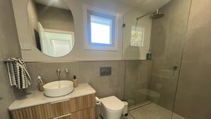 Ein modernes Badezimmer mit runder Spüle, Holzwaschtisch, Toilette und einer Duschkabine.
