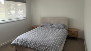 Ein Schlafzimmer mit einem Bett, zwei Nachttischen, einem Fenster und Blick ins Freie.