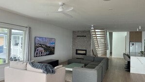 Ein modernes Wohnzimmer mit einer Couch, einem Couchtisch und einem Fernseher. Eine Treppe führt zu einer Küchenzeile.