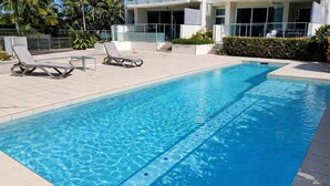 Une piscine avec des chaises longues et un bâtiment moderne en arrière-plan.