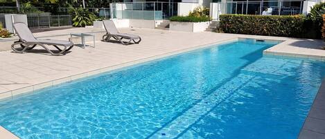 A swimming pool with lounge chairs and a modern building in the background.