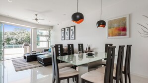 Un espace de salle à manger moderne avec une table en verre, des chaises foncées et des luminaires suspendus.
