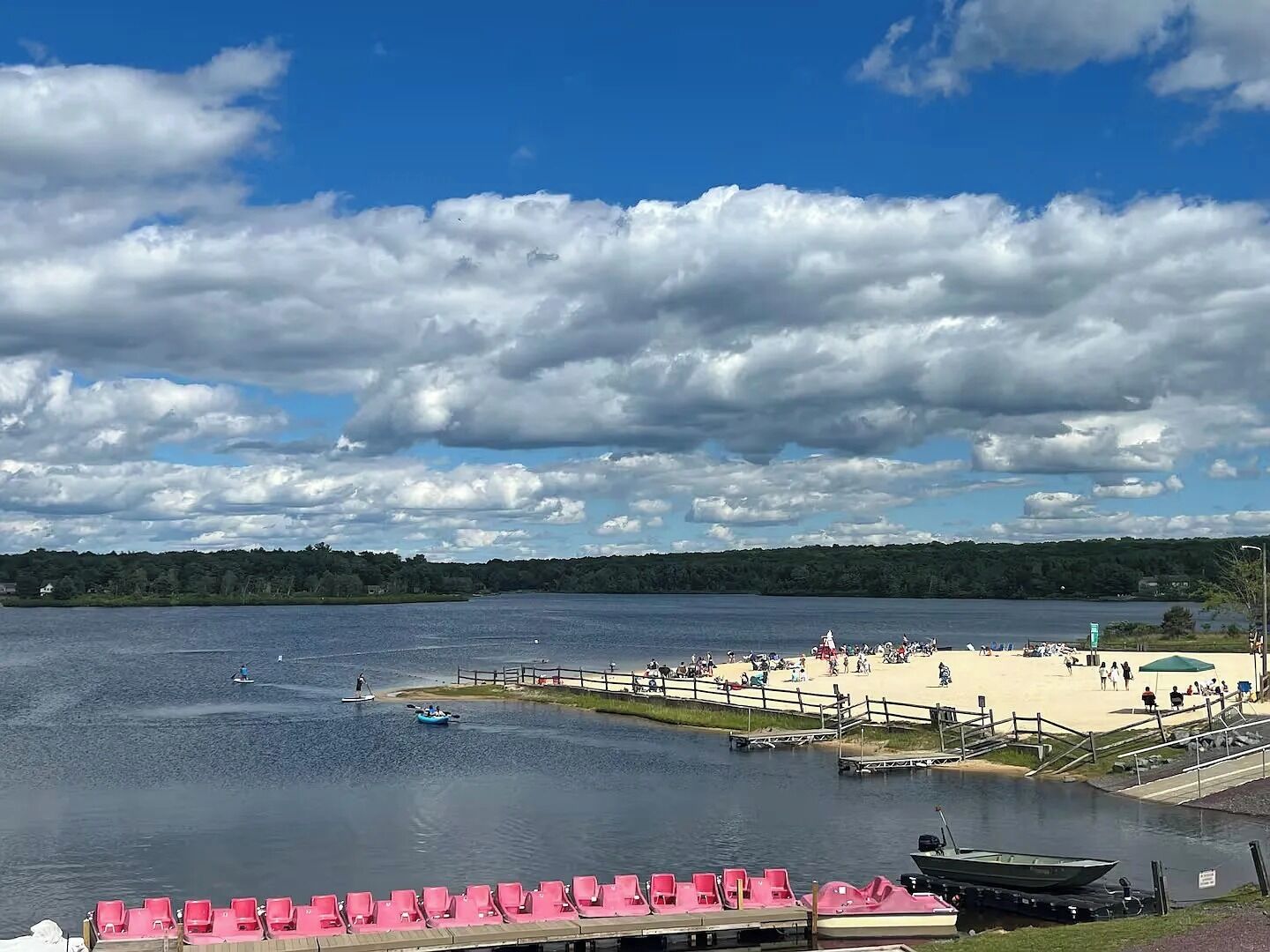 Näkymä järvelle, jossa on hiekkaranta, soutuveneitä ja rivi vaaleanpunaisia tuoleja.
