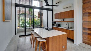 A modern kitchen with a central island, bar stools, a ceiling fan, and a view of greenery outside. - Rhys Apartment - Berawa (Canggu)